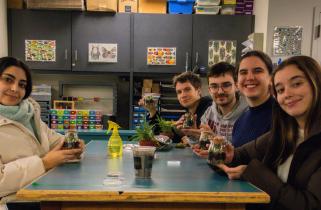 Group of students sits around a class table full of newly-built terrarium jars